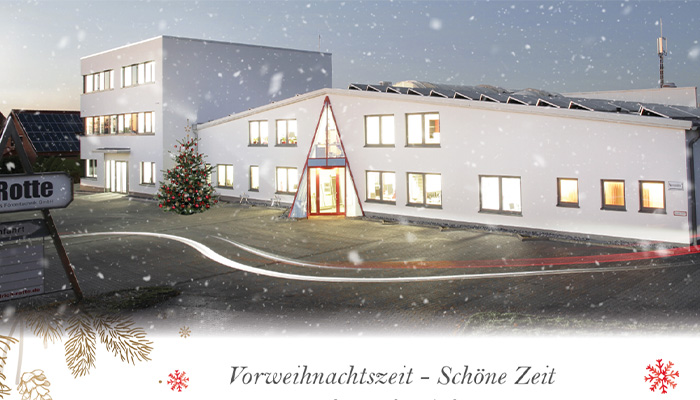 Firmengebäude in leicht verschneiter Winterlandschaft mit Weihnachtsbaum vor dem Eingang und beleuchteten Fenstern bei Dämmerung