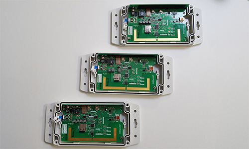 Drei offene elektronische Gehäuse mit grünen Leiterplatten und verschiedenen Komponenten, auf hellem Untergrund angeordnet.