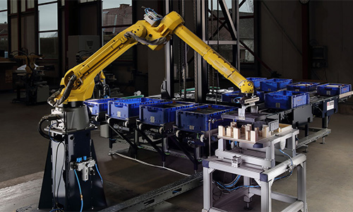 Gelber Industrieroboterarm in einer Fabrikumgebung, der Objekte von blauen Plastikbehältern auf ein Förderband oder eine Tischfläche bewegt.