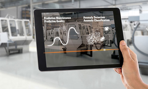 Hand hält Tablet mit Anzeige von Datenanalyse-Visualisierungen vor einer Fabrikhalle mit Fertigungsmaschinen
