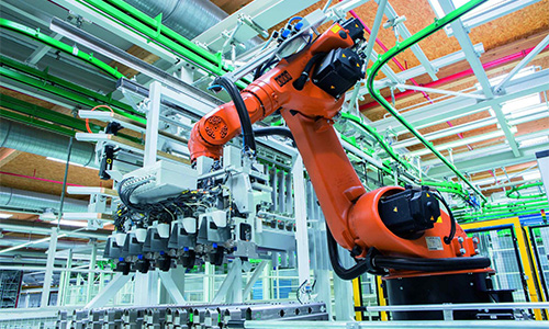 Industrieroboterarm mit Greifvorrichtung in einer modernen Fertigungsanlage mit grünen Rohren und strukturiertem Deckenhintergrund
