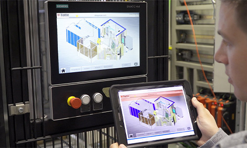 Nahaufnahme einer Person, die ein Tablet mit einer 3D-anwendung hält, während im Hintergrund ein Siemens Industrie-Monitor mit derselben 3D-Darstellung sichtbar ist, in einem technischen oder industriellen Umfeld.