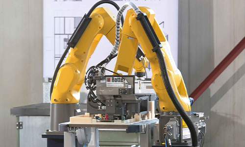 Zwei gelbe Industrieroboterarme, die an einer Maschine in einem Produktionsumfeld arbeiten
