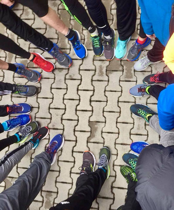 Viele Menschen stehen im Kreis auf gepflastertem Boden und tragen bunte Sportschuhe, nur die Beine und Füße sind sichtbar.