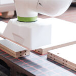 Roboterarm bearbeitet präzise Holzplatten mit Lasermessfeld auf Arbeitstisch in moderner Fertigungsumgebung