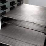 Drei übereinander liegende Metallplatten in einem Industrie- oder Maschinenumfeld, umgeben von Zahnketten und unterstützenden Metallstrukturen