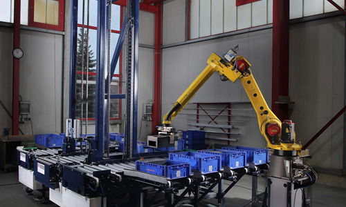 Gelber Industrieroboterarm in einer Fabrikumgebung, der blaue Kunststoffkisten auf einem Förderband bewegt.