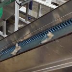 Förderband mit blauen Kunststoffzähnen und Metallrahmen in einer Fabrikumgebung.