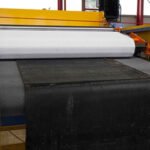 Maschine in einer Fabrik, die schwarzen und weißen Stoffmaterialien auf ein Förderband legt.