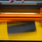 Oranger Zylinderapparat in einer gelben Maschine, der ein schwarzes Objekt schnell bewegt, sichtbar durch Bewegungsunschärfe.