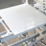 Metalltisch mit glänzender weißer Oberfläche, eingebaut in eine Maschine mit Rollenförderern und mechanischen Komponenten in einer industriellen Umgebung