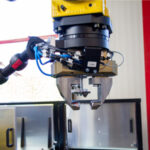 Industrieroboter mit Greifarm und pneumatischer Steuerung in einer Werkstattumgebung vor geöffneten Metallschränken