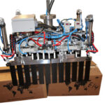 Industrieroboter mit mehreren pneumatischen oder hydraulischen Schläuchen und Greifern, positioniert über zwei Kartons mit Weltkartenaufdruck in weißem Raum