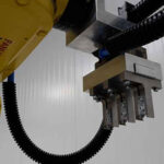 Gelber Industrieroboterarm mit Gelenk und Greifvorrichtung in einer industriellen Umgebung mit weißen Wänden