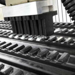 Nahaufnahme eines industriellen Geräts mit schwarzen, rechteckigen Kunststoffelementen auf zwei parallelen Schienen, umgeben von einem schwarzen flexiblen Schlauch und einem weißen oberen Teil.