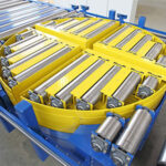 Rundförderer mit gelben seitlichen Schutzvorrichtungen und mehreren silbernen Walzen zur Materialbeförderung in einer industriellen Umgebung