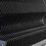 Nahaufnahme einer Reihe gleichmäßig geformter, schwarzer, gebogener Lamellen oder Lamellenstruktur mit Schrauben an der Seite