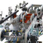 Industrielle Produktionsanlage oder Förderbandsystem mit Metallrahmen, Zahnrädern, Sensoren und elektrischen Kabeln vor weißem Hintergrund