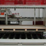 Industriemaschine mit Förderrollen und einem flachen Holzbretter-Paket als Fördergut auf dem Transportband in einer Fabrikumgebung