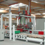 Moderne industrielle Produktionsanlage mit automatisierten Förderbändern, Greifarmen und Steuerungskonsole in einer hellen Fabrikumgebung