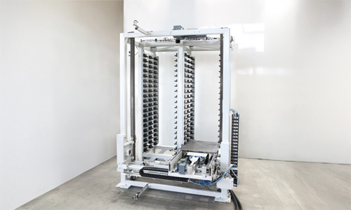 Große weiße industrielle Maschine mit Metallgestell und mehreren vertikalen Reihen von kleinen schwarzen Halterungen in einem hellen, leeren Raum mit Betonboden und weißen Wänden.