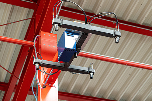 Nahaufnahme einer industriellen Kamera oder Sensorsystem an einem roten Stahlträger unter einem Dach mit Metallplatten