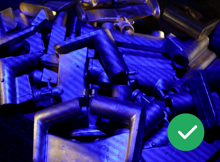 Mehrere metallische, rechteckige Teile mit abgewinkelten Griffen, die unter blauem Licht liegen.