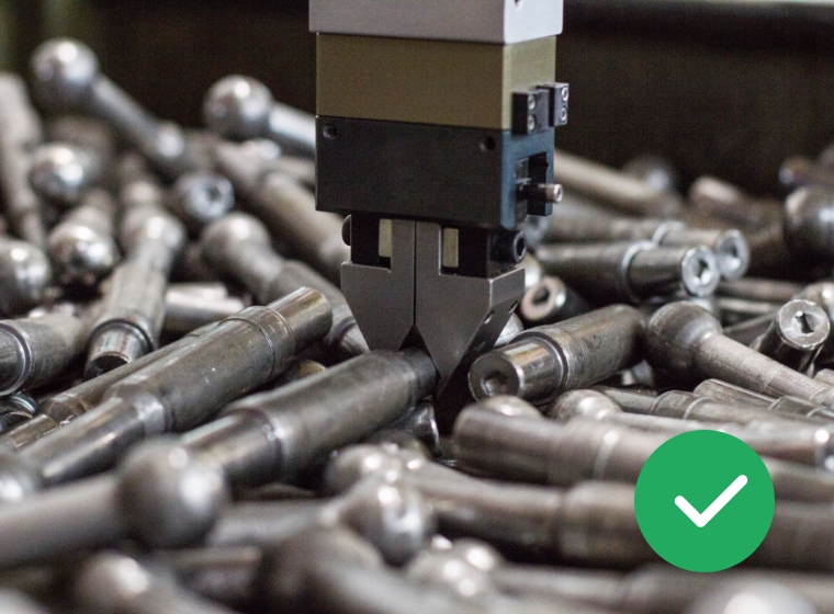 Roboterarm mit Greifzange, der Metallstifte oder Bolzen aus einem Haufen ähnlicher Teile aufnimmt