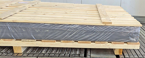 Holzpalette mit gestapelten Platten, die mit einer undurchsichtigen Folie umwickelt sind, in einem industriellen Lagerraum