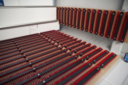 Nahaufnahme von Reihen roter und schwarzer Kunststoffteile auf einem weißen Tisch, die in einem Raum mit grauem Boden und weißen Wänden angeordnet sind