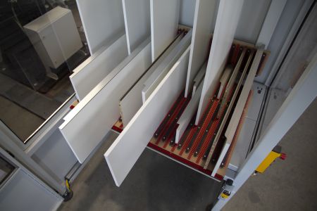 Ansicht von schräg oben auf mehrere weiße rechteckige Platten, die in einem industriellen Gerät oder Förderanlage mit Rollenbahnen abgesenkt oder sortiert werden.