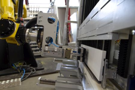 Industrieroboter mit Greifarm, der ein größeres metallisches Bauteil in einer Fertigungsanlage hält.