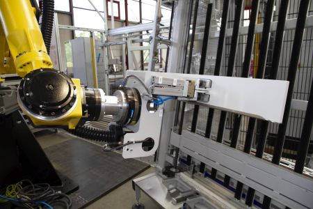 Gelber Roboterarm in einer industriellen Produktionsumgebung, der an einer weißen Maschinenkonstruktion arbeitet
