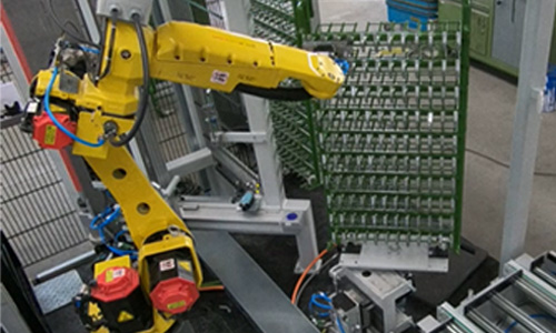 Gelber Industrieroboterarm in einer Fertigungsanlage, umgeben von Förderbändern und Metallgestellen