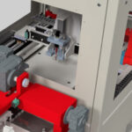 Detailaufnahme einer industriellen Maschine mit grauer und roter Metallkonstruktion und beweglichen mechanischen Komponenten in einem geschlossenen Gehäuse.
