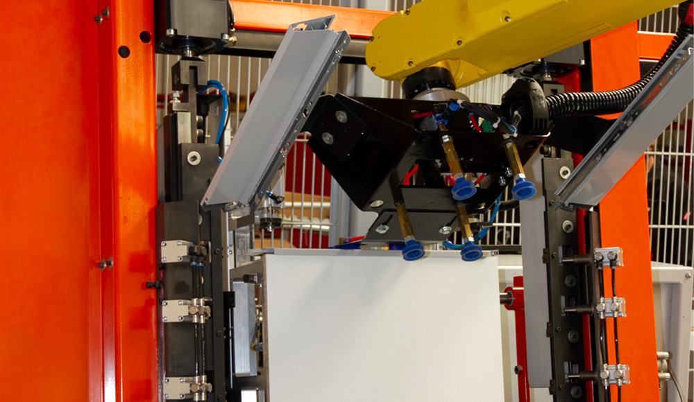 Gelber Industrieroboterarm mit Greifern und Saugnäpfen, der eine weiße Platte in einem orangefarbenen Maschinenrahmen hält, umgeben von Metallstreben und elektrischen Kabeln.