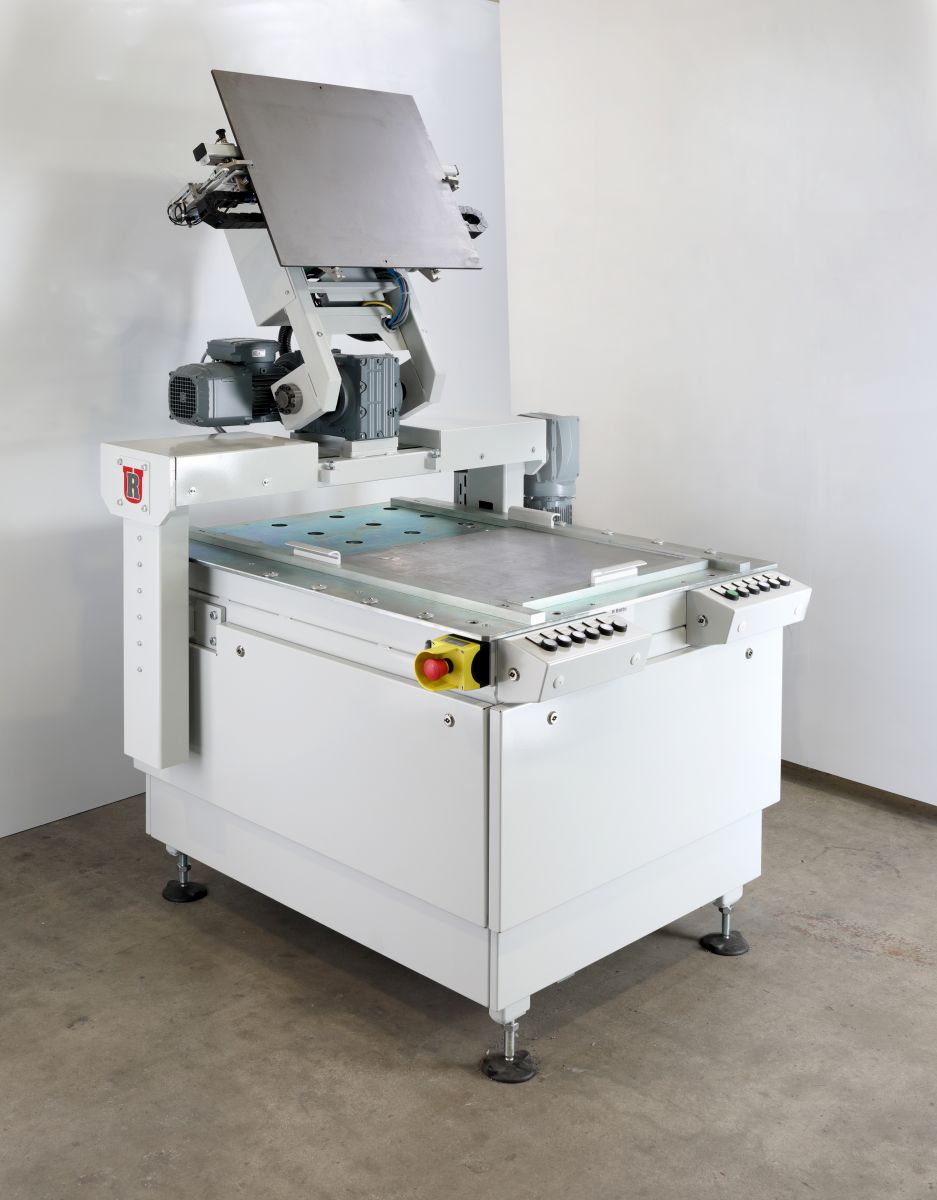 Industrielle weiße Maschine mit großer flacher Arbeitsfläche und Motorarm in einer Werkstatt mit weißem Hintergrund.