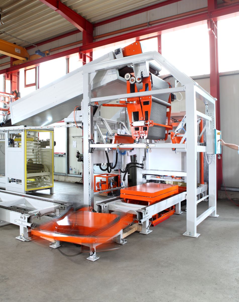 Industriemaschine mit orangefarbenen Förderbändern und Fördertechnik in einer Fabrikhalle mit Betonboden und Fensterfront