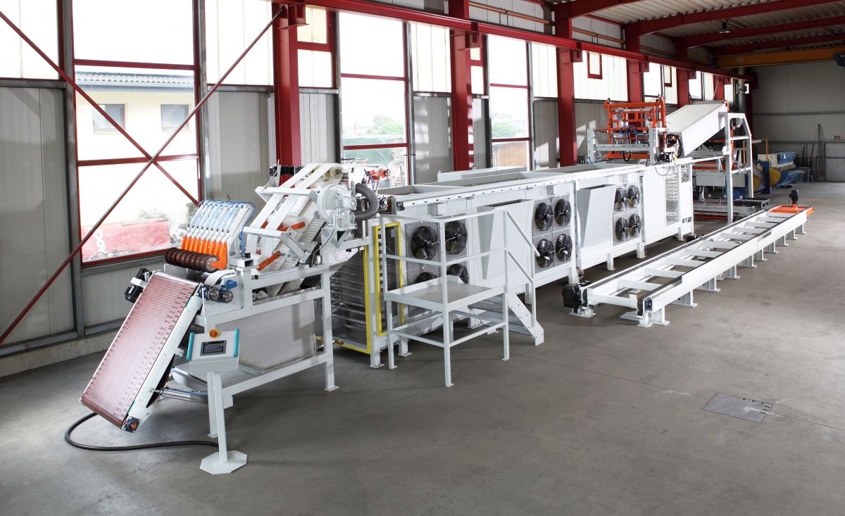 Große industrielle Verpackungsmaschine mit Förderband und Lüftern in einer Halle mit roten Stahlträgern.