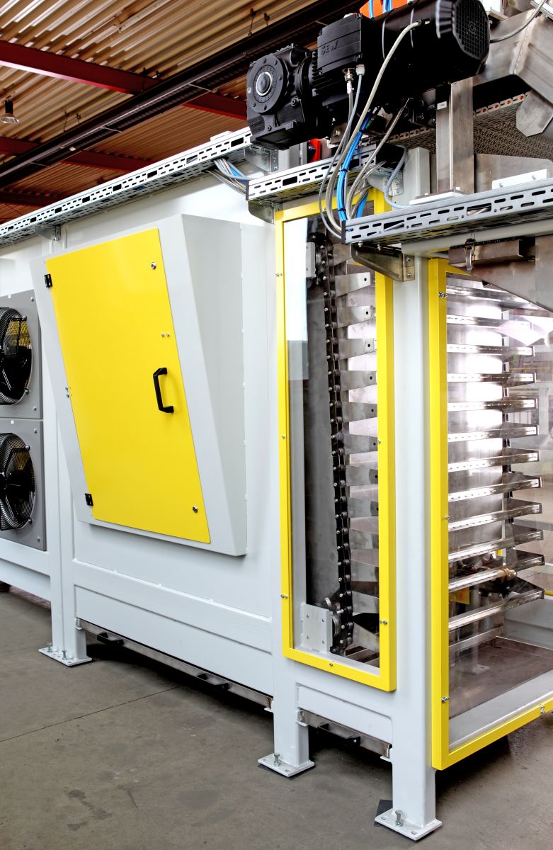 Industriemaschine mit gelbem Bedienfeld und mehreren Metallbändern in einem Produktionsumfeld mit Betonboden und Stahlträgern.