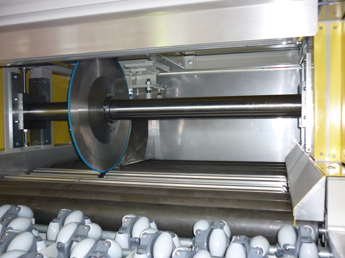 Maschineninnenraum mit einer großen rotierenden Scheibe und mehreren weißen, walzenartigen Bauteilen im Vordergrund