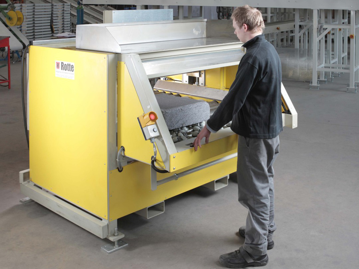 Mann bedient gelbe industrielle Maschine mit grauem Schaumstoffelement in Werkstattumgebung.