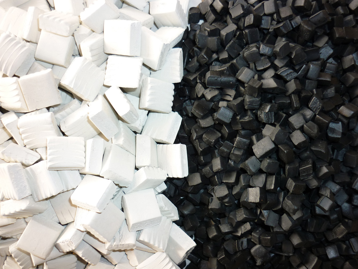 Schwarze und weiße quadratische Kunststoffgranulatstücke nebeneinander auf einer Oberfläche verteilt.