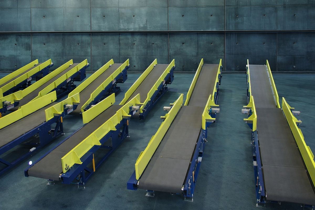 Mehrere schräge Förderbänder mit gelben Seitenwänden in einer Halle mit grauen Wänden und Boden