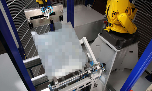 Gelber Industrieroboterarm in Käfig montiert, der ein unscharfes Objekt mit Greifmechanismus hält.