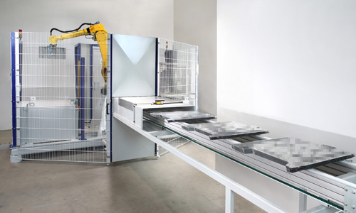 Industrieroboter verlädt rechteckige Metallplatten auf ein Förderband in einer Halle mit weißer Wand.