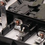 Nahaufnahme von Metallkontakten in einem schwarzen Batteriefach mit sichtbaren Schrauben und Kunststofftrennwänden.