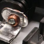 Nahaufnahme eines Metallklemmenverschlusses mit Schraube auf einem schwarzen Kunststoffteil