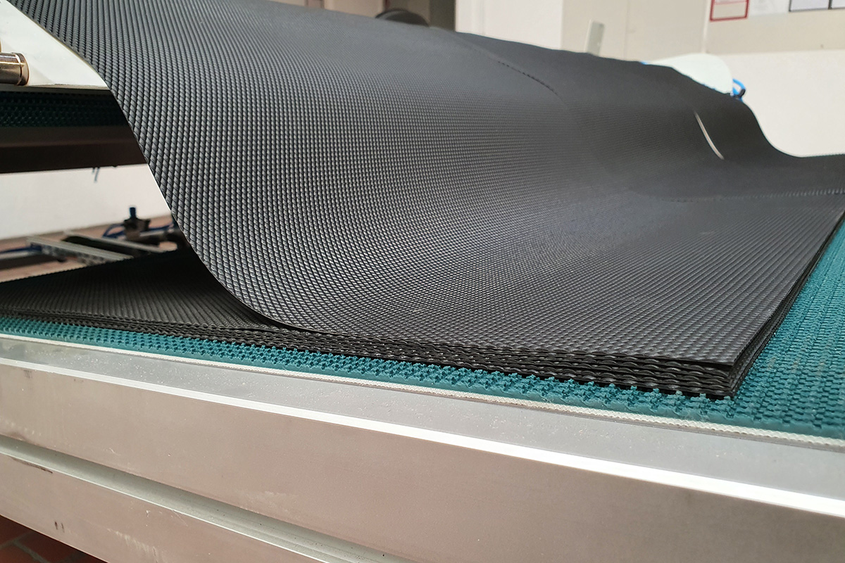 Schwarzes, texturiertes Material mit Wabenmuster auf einer Tischfläche aus Metall und grünem Teppich.